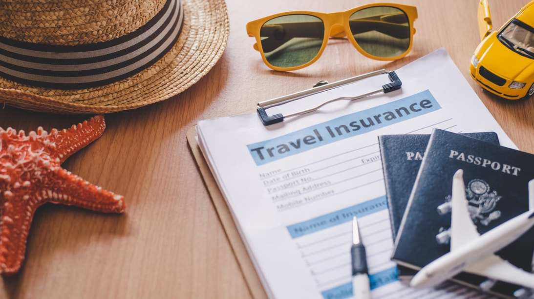 Passports and a form for Travel Insurance on a table surrounded by a hat, sunglasses and a starfish. 