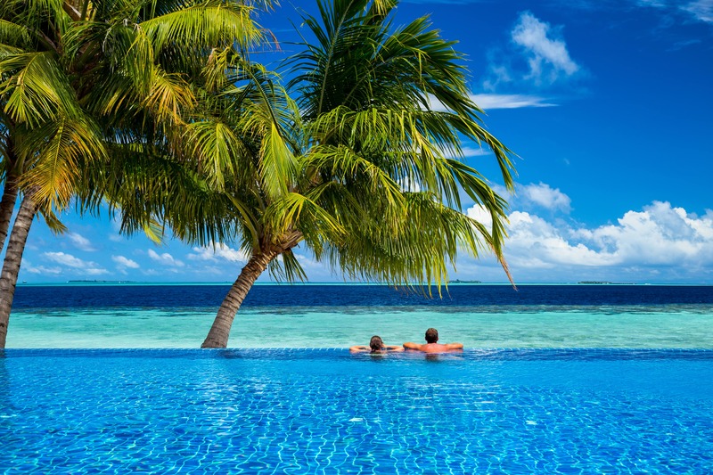 Couple relaxing in tropical infinity pool under palm trees